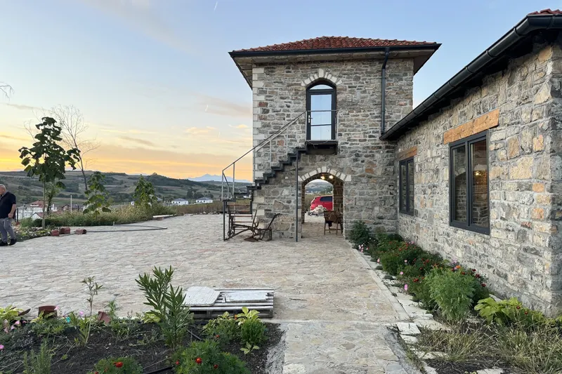 The stone tower and courtyard at sunset, with green hills and mountains behind