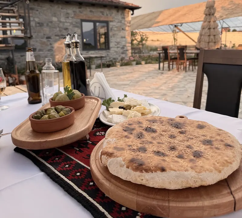 A round loaf of bread on a wooden board on the terrace table, with olives and cheese