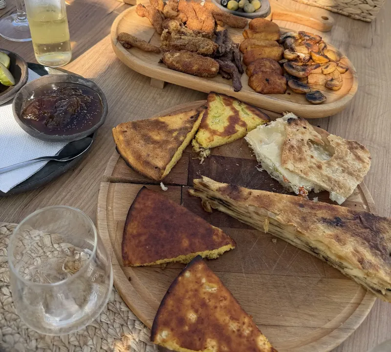 Slices of savoury pie and golden cornbread on wooden boards, with a platter of fried starters