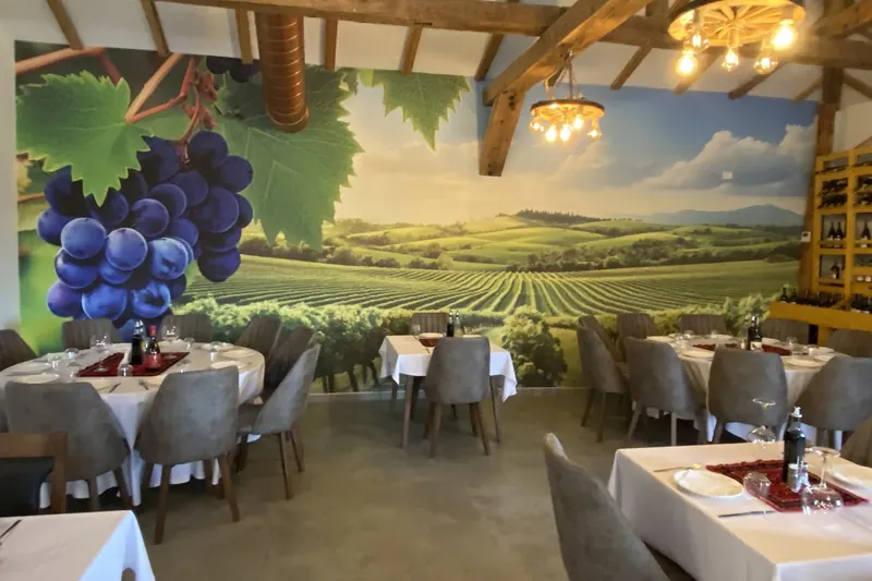 The dining hall under wooden beams, with a vineyard and grape mural across the wall