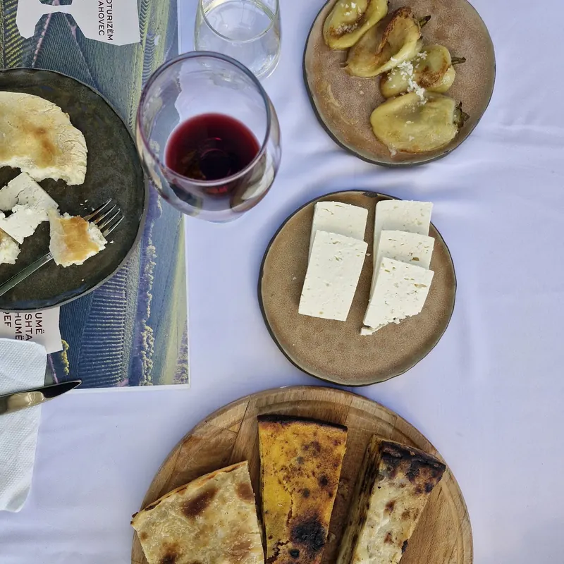 A table seen from above: red wine, white cheese, baked peppers and slices of pie