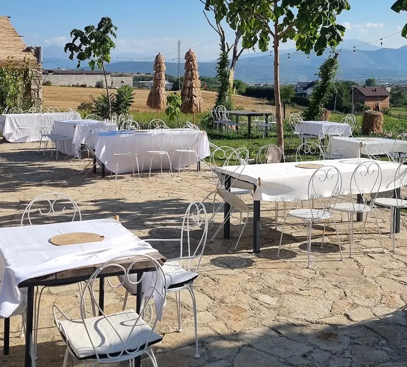 The stone terrace with white tablecloths, wrought-iron chairs, young trees and mountains on the horizon